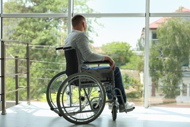 Photo of Young man in wheelchair near window indoors