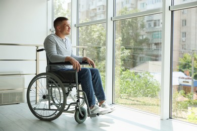 Photo of Young man in wheelchair near window indoors