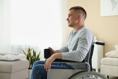 Photo of Young man with cup of drink in modern wheelchair at home