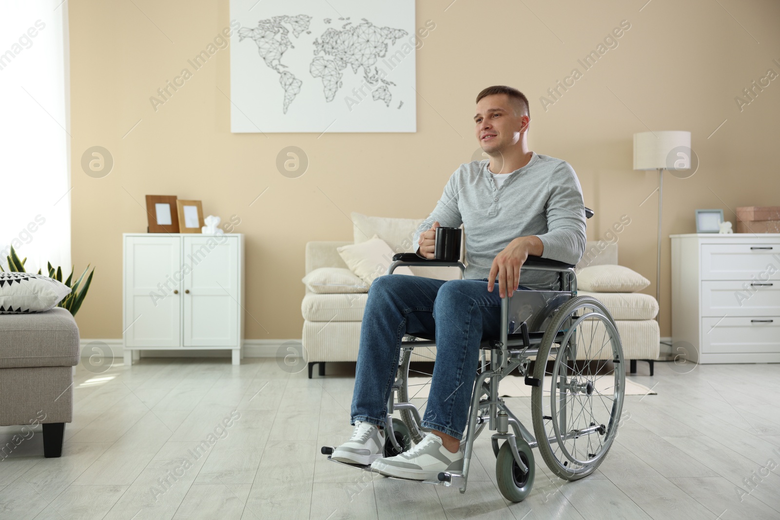 Photo of Young man with cup of drink in wheelchair at home, space for text