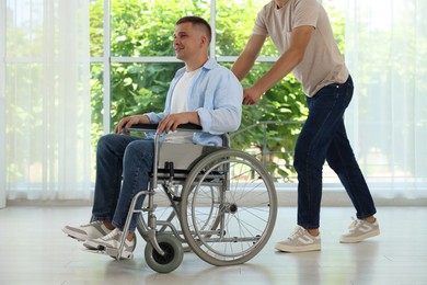 Photo of Caregiver with man in wheelchair near window indoors, closeup