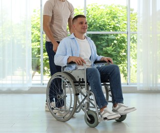 Photo of Caregiver with man in wheelchair near window indoors, closeup