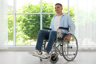 Photo of Young man in wheelchair near window indoors