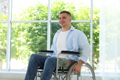 Photo of Young man in wheelchair near window indoors