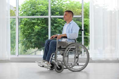 Photo of Young man in wheelchair near window indoors