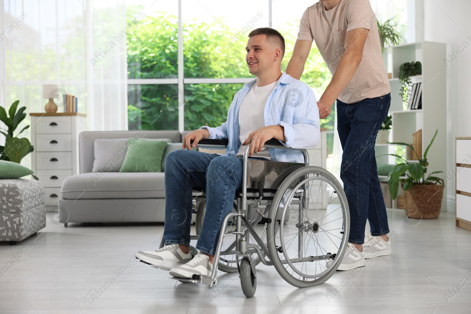 Photo of Caregiver with man in wheelchair near window indoors, closeup