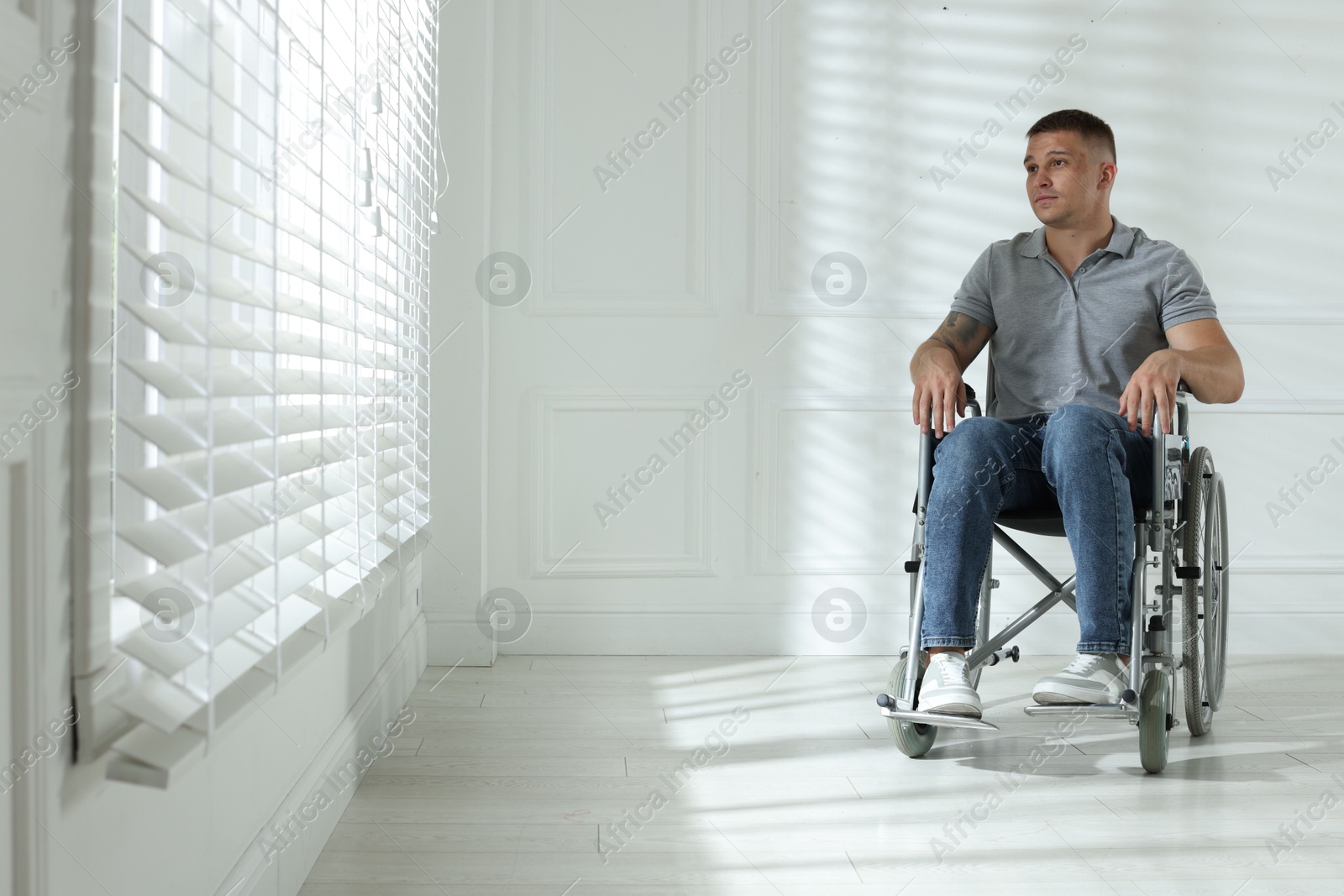 Photo of Young man in wheelchair near window indoors, space for text