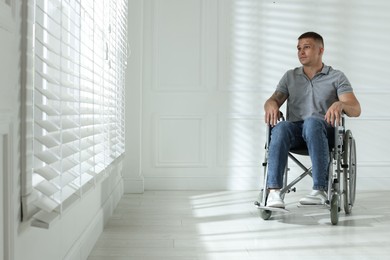 Photo of Young man in wheelchair near window indoors, space for text