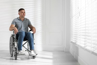 Photo of Young man in wheelchair near window indoors, space for text