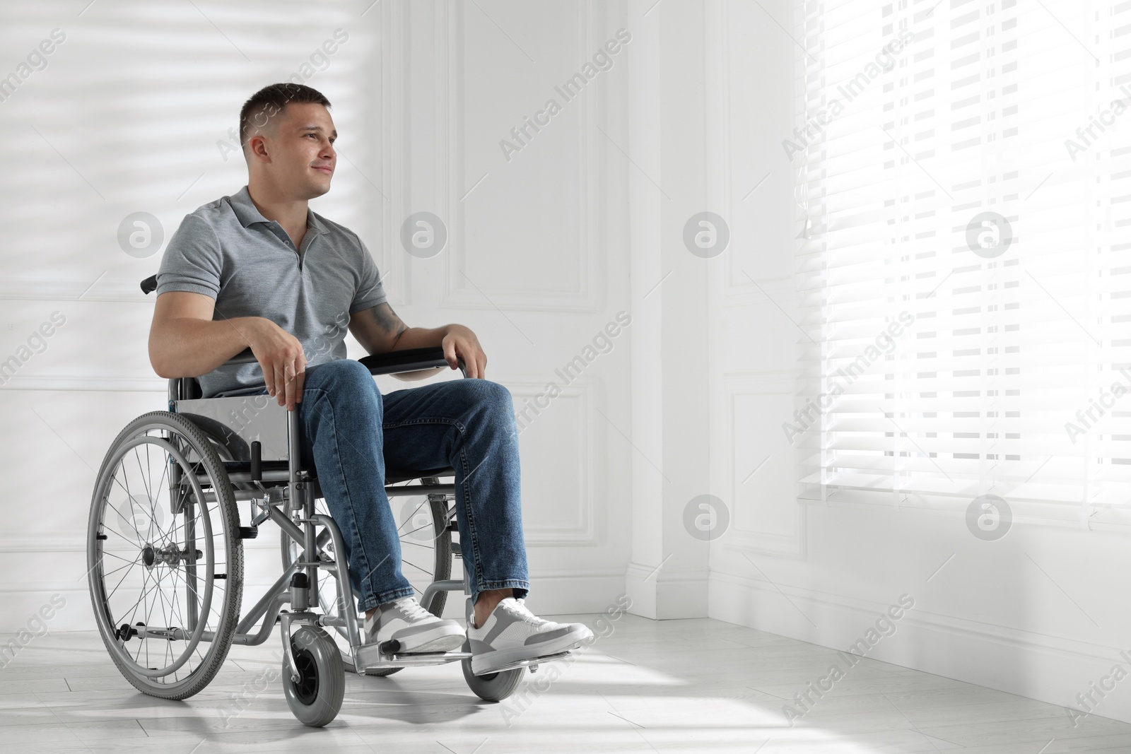 Photo of Young man in wheelchair near window indoors, space for text