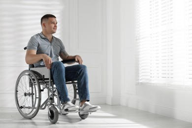 Photo of Young man in wheelchair near window indoors, space for text