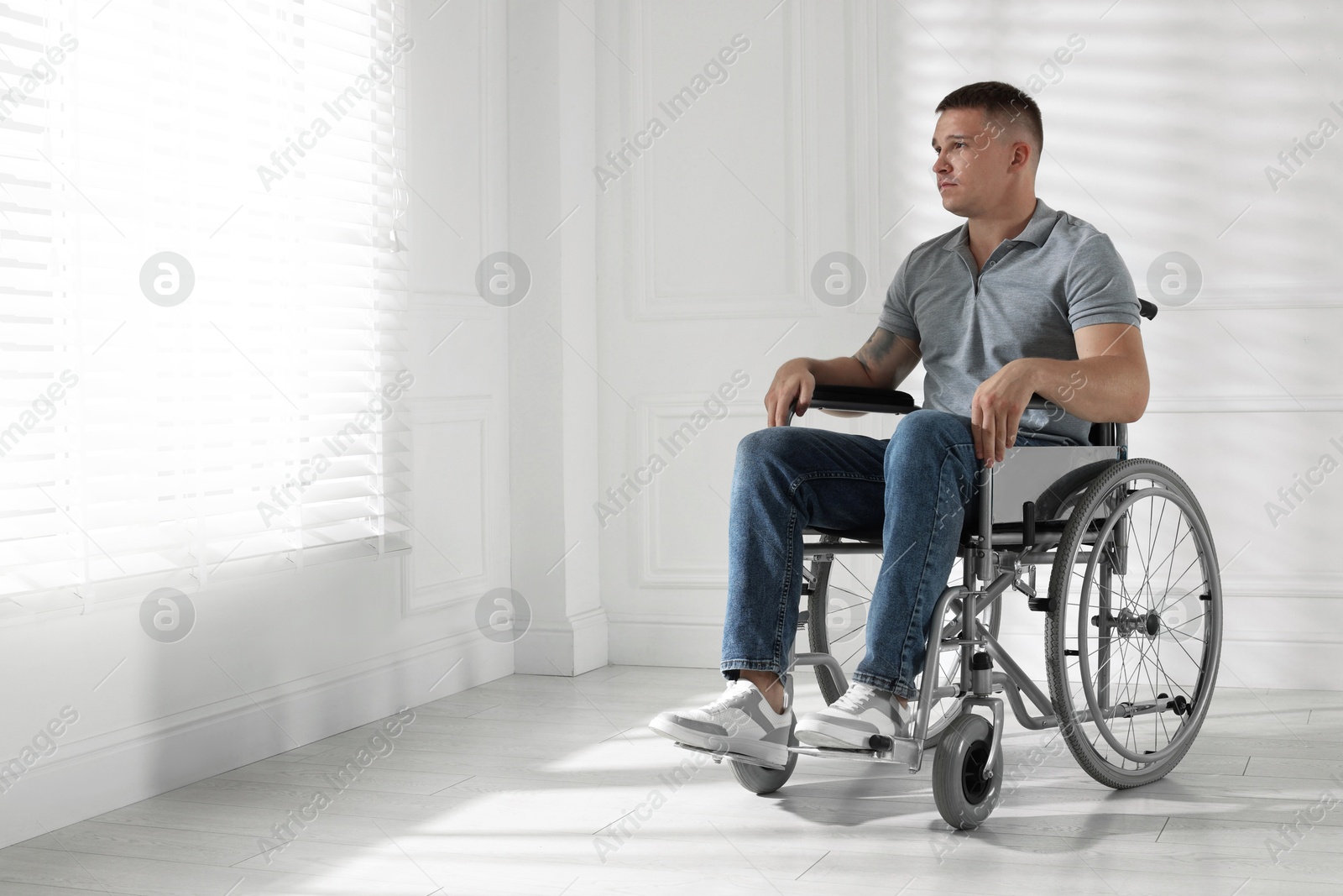Photo of Young man in wheelchair near window indoors, space for text