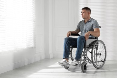Photo of Young man in wheelchair near window indoors, space for text