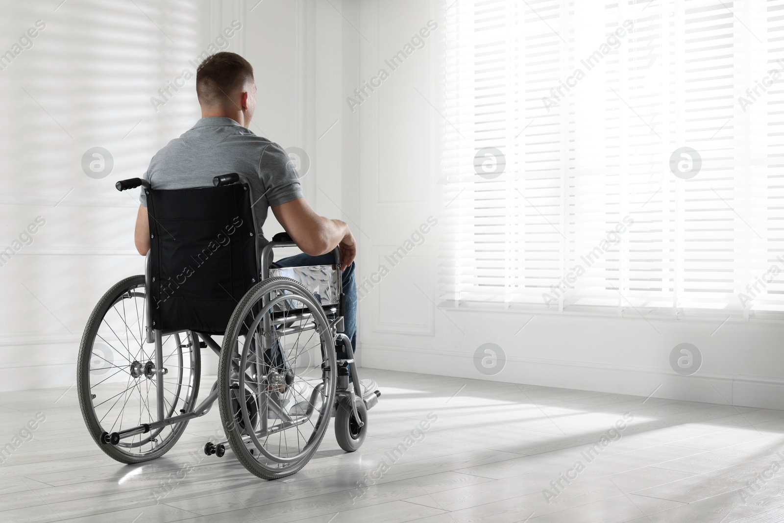 Photo of Young man in wheelchair near window indoors, space for text