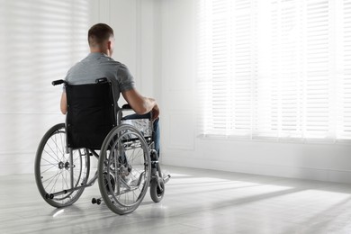 Photo of Young man in wheelchair near window indoors, space for text