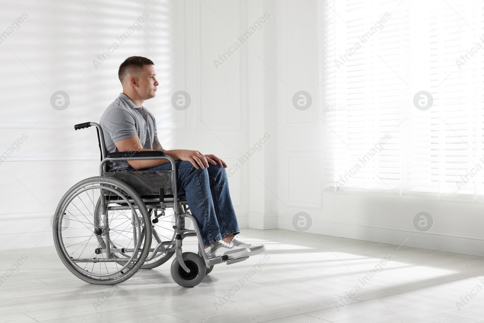 Photo of Young man in wheelchair near window indoors, space for text