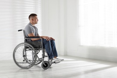 Photo of Young man in wheelchair near window indoors, space for text