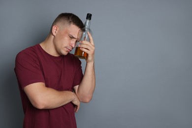 Photo of Man with bottle of whiskey suffering from hangover on grey background, space for text