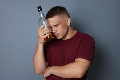 Photo of Man with bottle of whiskey suffering from hangover on grey background