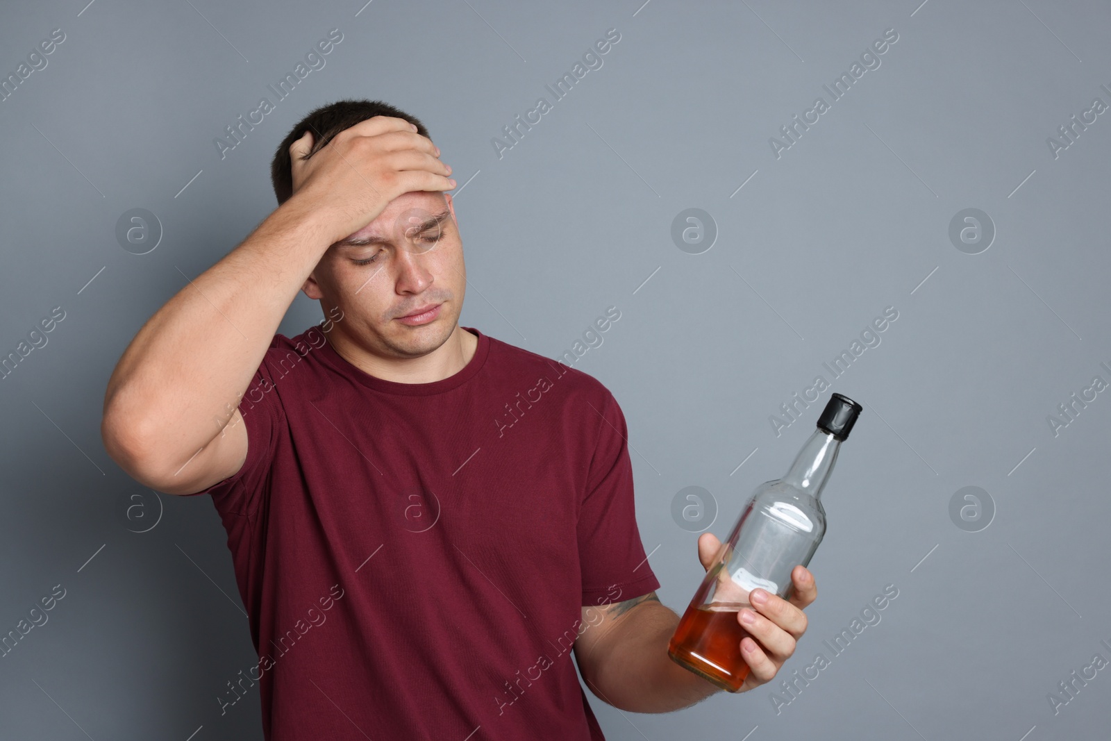 Man with bottle of whiskey suffering from hangover on grey background Photo of Man with bottle of whiskey suffering from hangover on grey background