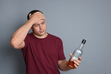 Photo of Man with bottle of whiskey suffering from hangover on grey background