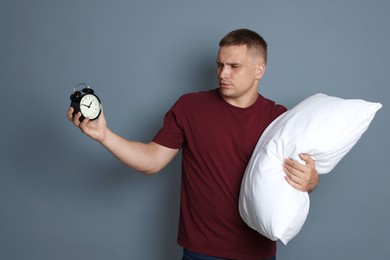 Photo of Man with alarm clock and pillow suffering from hangover on grey background