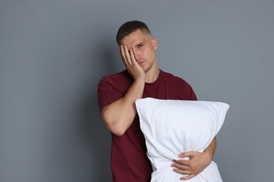 Photo of Man with pillow suffering from hangover on grey background