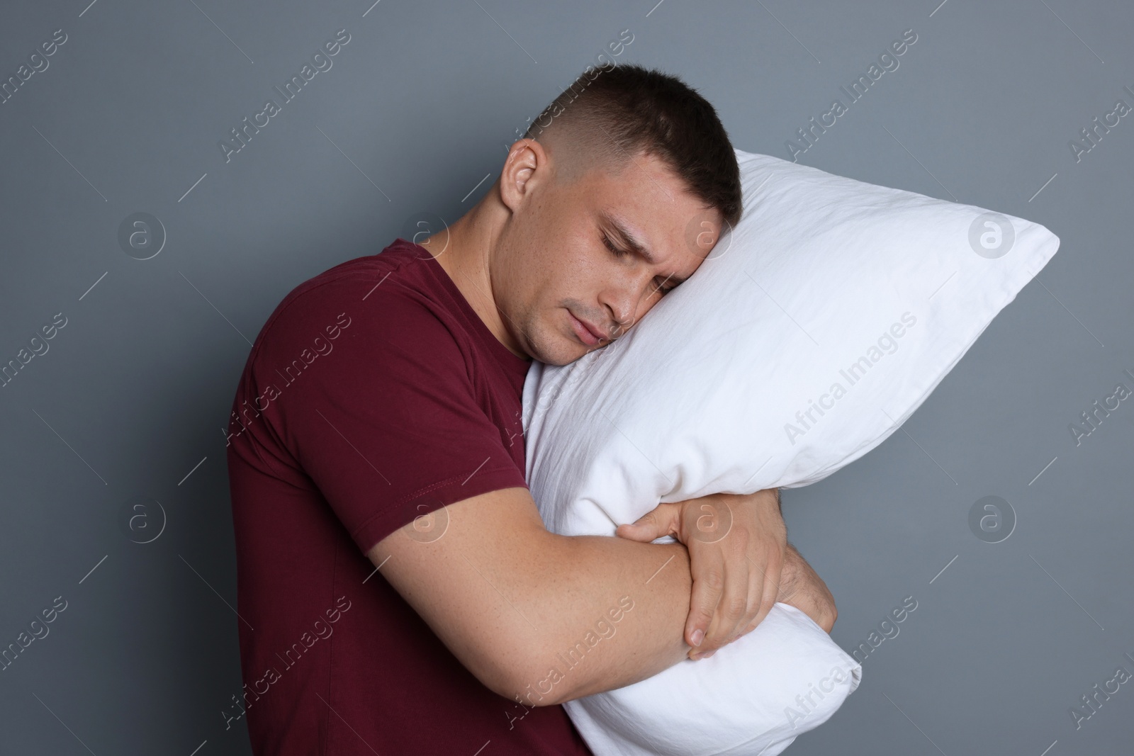 Man with pillow suffering from hangover on grey background Photo of Man with pillow suffering from hangover on grey background
