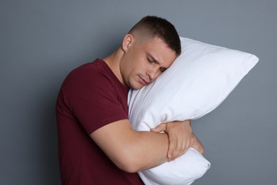Photo of Man with pillow suffering from hangover on grey background