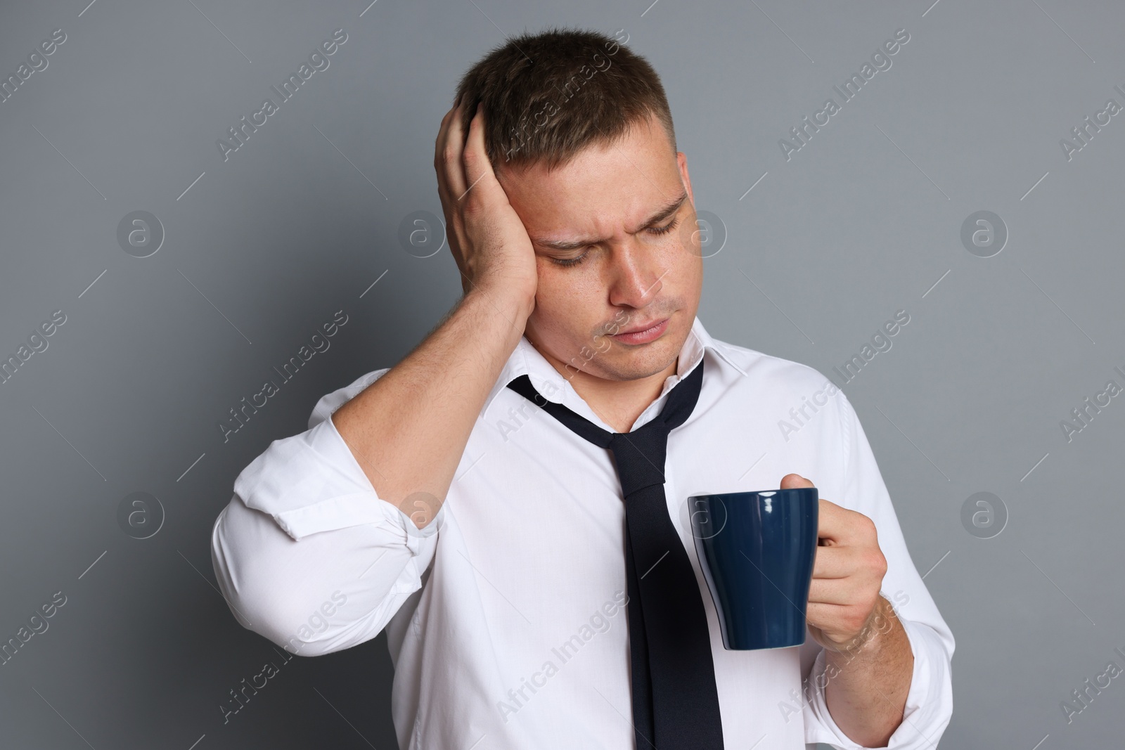 Man with cup of drink suffering from hangover on grey background Photo of Man with cup of drink suffering from hangover on grey background