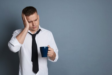 Photo of Man with cup of drink suffering from hangover on grey background, space for text