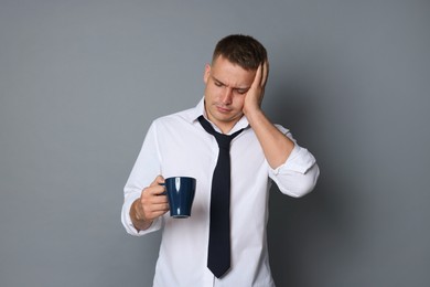Photo of Man with cup of drink suffering from hangover on grey background
