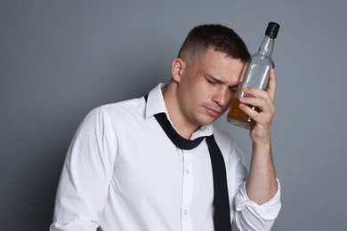 Photo of Man with bottle of whiskey suffering from hangover on grey background