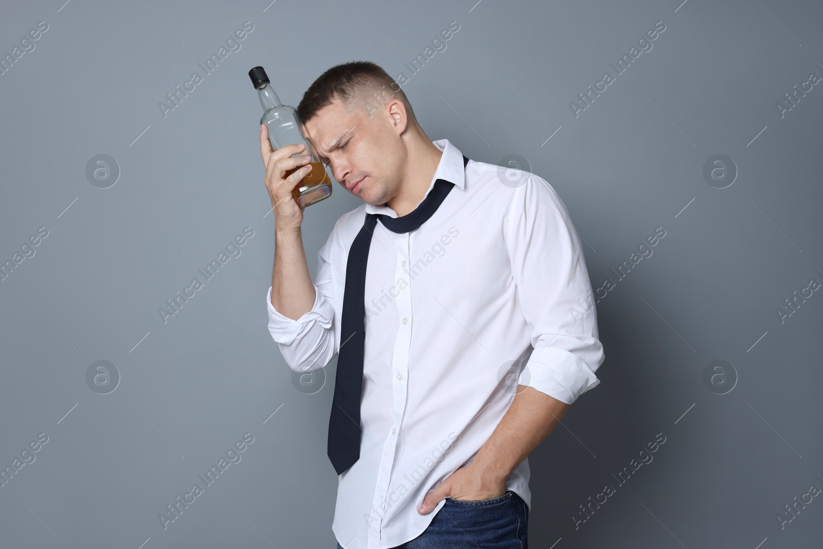 Man with bottle of whiskey suffering from hangover on grey background Photo of Man with bottle of whiskey suffering from hangover on grey background