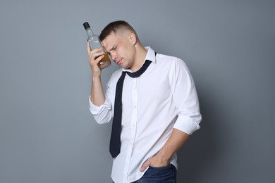 Photo of Man with bottle of whiskey suffering from hangover on grey background