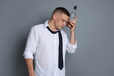 Photo of Man with bottle of whiskey suffering from hangover on grey background