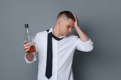 Photo of Man with bottle of whiskey suffering from hangover on grey background