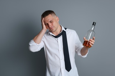 Photo of Man with bottle of whiskey suffering from hangover on grey background