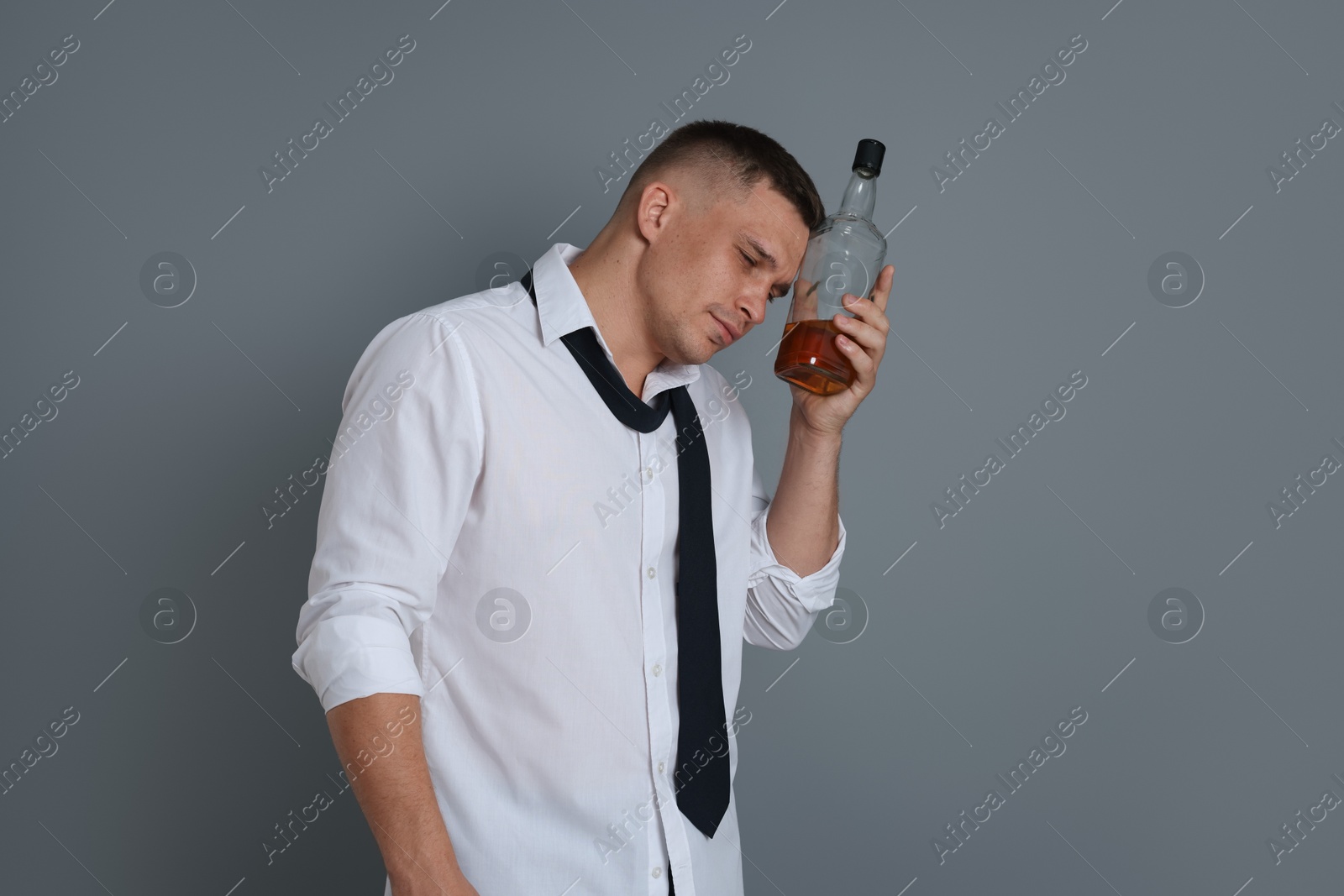 Man with bottle of whiskey suffering from hangover on grey background Photo of Man with bottle of whiskey suffering from hangover on grey background