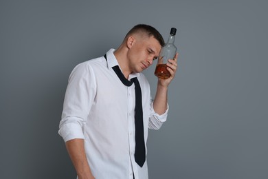 Photo of Man with bottle of whiskey suffering from hangover on grey background