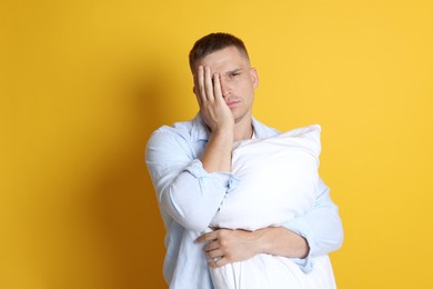 Photo of Man with pillow suffering from hangover on orange background