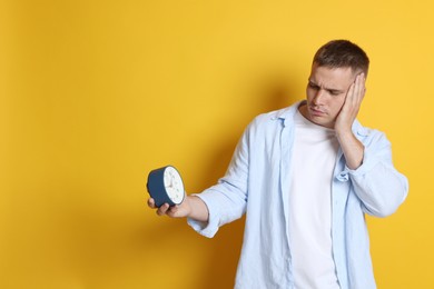 Photo of Man with alarm clock suffering from hangover on orange background, space for text
