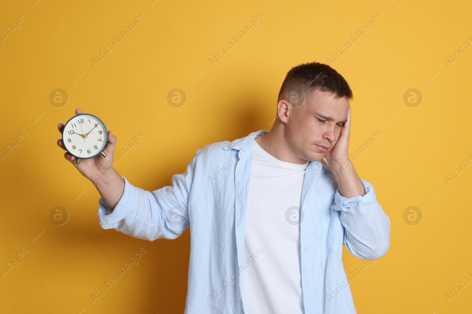 Man with alarm clock suffering from hangover on orange background Photo of Man with alarm clock suffering from hangover on orange background