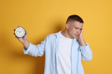 Photo of Man with alarm clock suffering from hangover on orange background