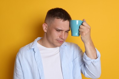 Photo of Man with cup of drink suffering from hangover on orange background