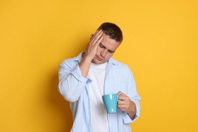 Photo of Man with cup of drink suffering from hangover on orange background