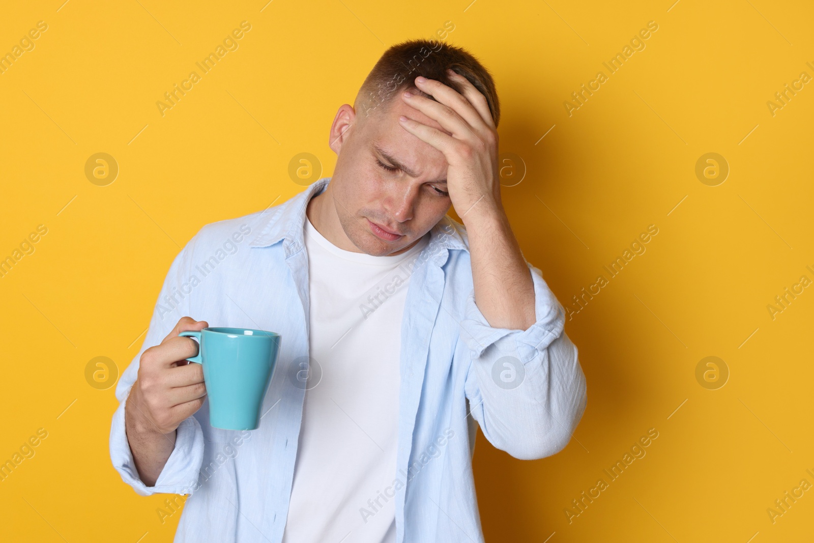 Man with cup of drink suffering from hangover on orange background Photo of Man with cup of drink suffering from hangover on orange background