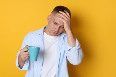 Photo of Man with cup of drink suffering from hangover on orange background