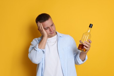 Photo of Man with bottle of whiskey suffering from hangover on orange background