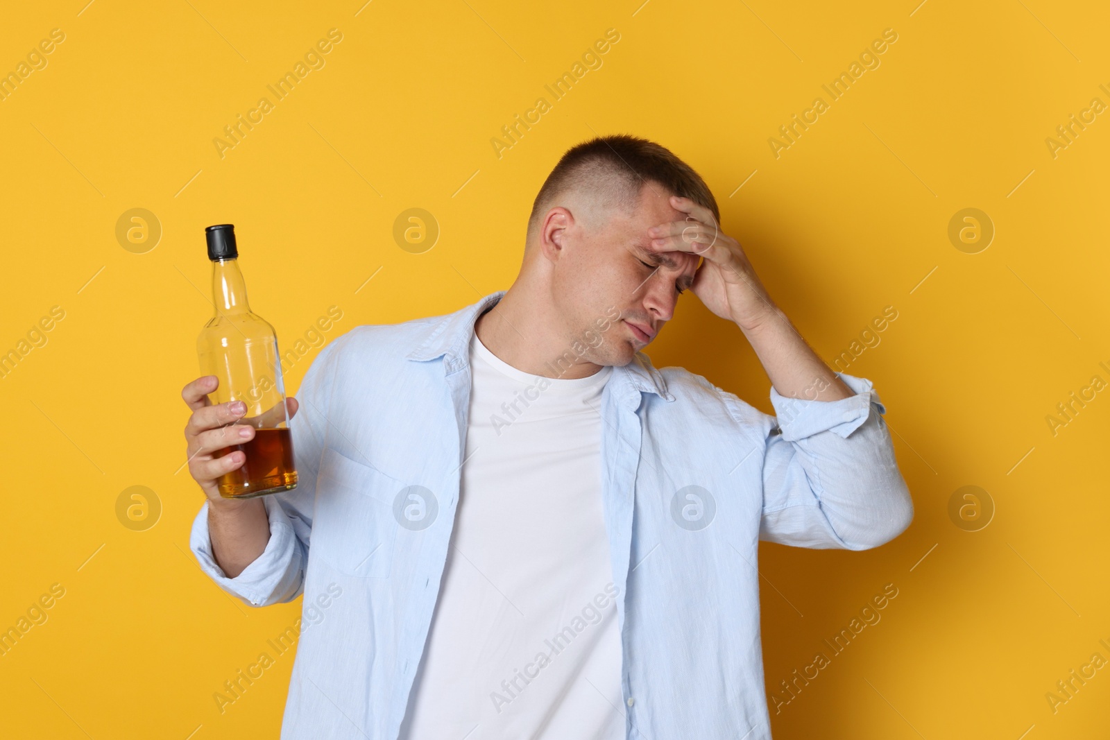 Man with bottle of whiskey suffering from hangover on orange background Photo of Man with bottle of whiskey suffering from hangover on orange background